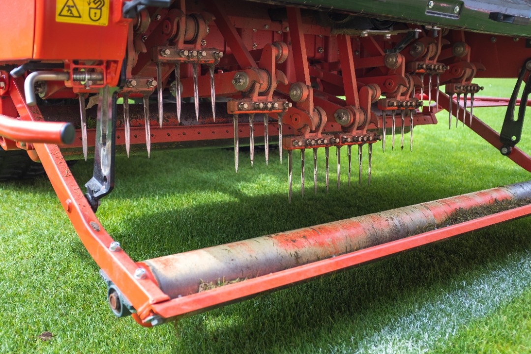 Close-up view of a professional aerator with sharp tines used for relieving soil compaction and improving turf health on grass.